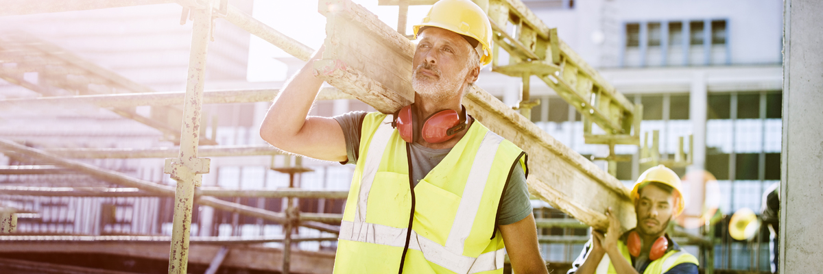 Construction worker carrying wooden beam at construction site.